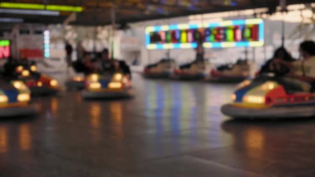 Blurred and unfocused footage of unrecognizable happy crowd enjoying amusement park rides on summere time holiday break, bumper cars ridden by kids and parents, laughing and shouting
