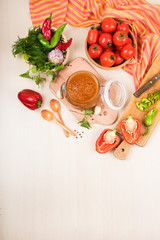 Tomato sauce (ketchup, adzhika) and vegetables on a beige table. Home preservation.