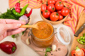 Tomato sauce (ketchup, adzhika) and vegetables on a beige table. Home preservation.