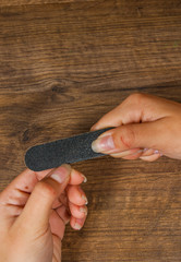 Fototapeta premium Hands on the table with manicure. Sawing makes the shape of the nail. on a wooden background. with copy space. top view