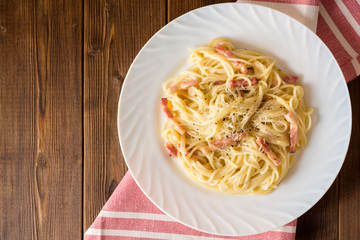 Classic pasta carbonara. Spaghetti with bacon, egg yolk and parmesan cheese on white plate on dark wooden background.