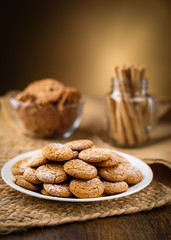 Honey ginger cookies in the foreground. Oatmeal raisin cookies and pirouette rolled wafers in the background.  Jute, burlap on wooden table. Warm home atmosphere.