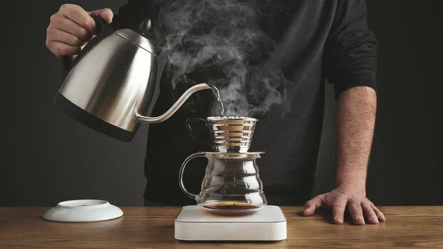 Cinemagraph of professional barista pourng not boiling water into coffee espresso french filter coffee pot, stands on scale, brewing energy caffeine drink, steam comes out