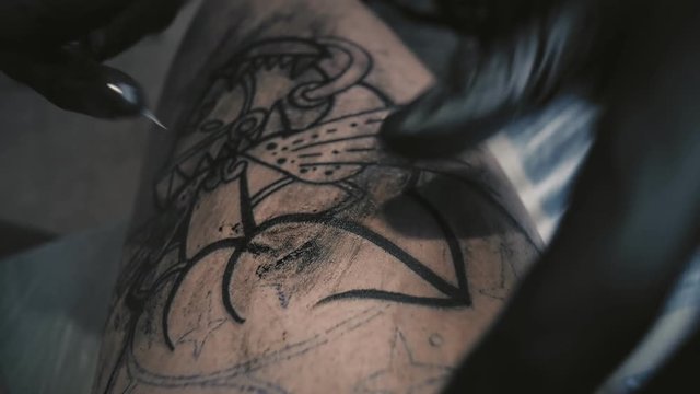 Close up macro view of tattooing process. Master makes contouring lines with his handmade professional liner machine on man leg, top view