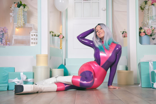 pretty anime girl wearing latex rubber doll catsuit and posing near cute white gift shop with air ballons and presents for christmas and new year