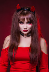 A beautiful, sexy woman in a devil costume, a demon with horns in a red dress. American, dress for a costume party Halloween. Choker on the neck. Bright makeup