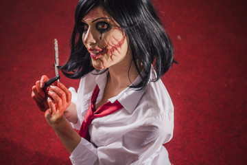 Zombie horror school girl holding a sharp razor, bloody and aggressive