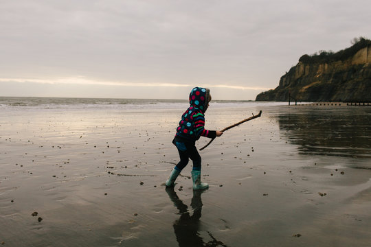 Little girl runs with a stick on a wet wintry beach in the morning.