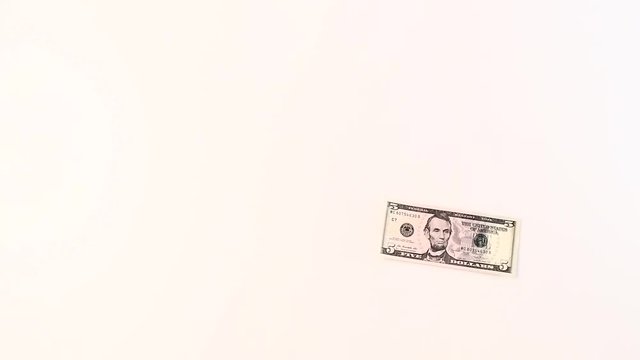 A five dollar bill is falling on a white background. Slow motion.