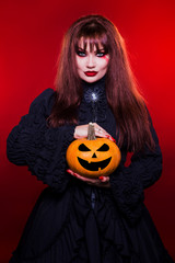 Beautiful woman, a witch, a vampire holding a pumpkin, on a red background. American, dress for a...