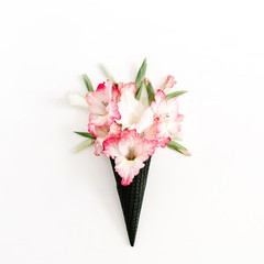 Black ice cream waffle cone with dry pink gladiolus flowers isolated on white background. Flat lay, top view flower concept.