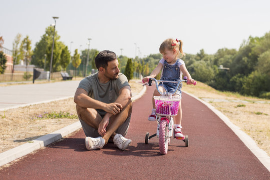 Young father teaching daughter to ride a bicycle on beautiful sunny day