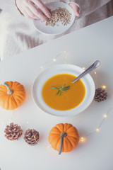 Pumpkin soup with rosemary in white plate near a pine cone with Fairy Ligths