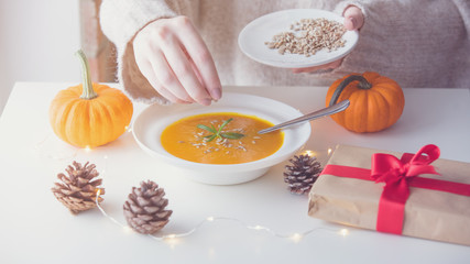 Pumpkin soup with rosemary in white plate near a pine cone with Fairy Ligths