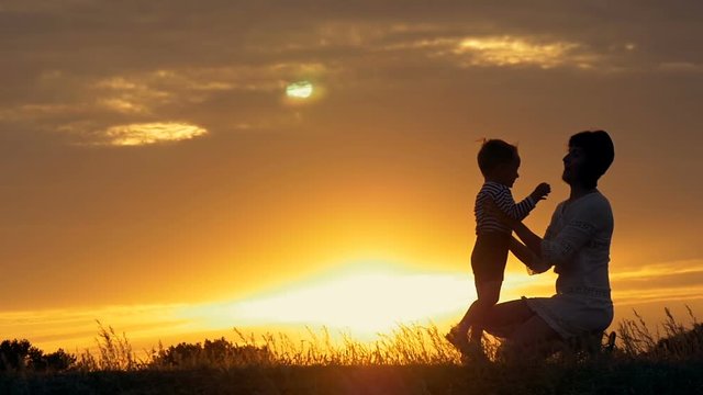 a silhouette of a happy young boy child running into the arms of his loving mother for a hug, in front of the sunset in the sky on a summer day.