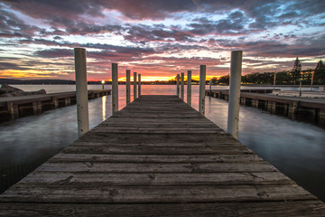 Wooden Dock On Sunrise Lake. Summer sunrise over the waters of Grand Traverse Bay in Traverse City, Michigan. Shot with long wooden dock in foreground sunrise over water at horizon.