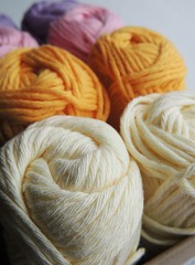 White, cream, yellow, pink and lilac cotton yarn balls for knitting and crocheting in box.
