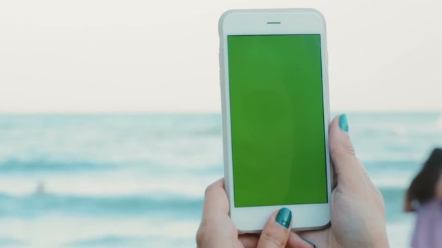 Closeup woman hand using smart phone green screen chromakey seaside horizon sea blurred background vacation internet surfing shopping digital technology female tapping pointing finger touchscreen
