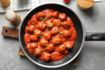 Frying pan with delicious meatballs in tomato sauce on table
