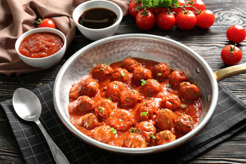 Saucepan with delicious meatballs in tomato sauce on table