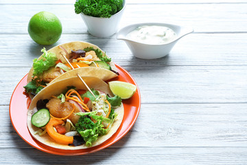 Plate with delicious fish tacos on wooden table