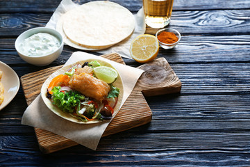 Wooden board with delicious fish taco on table