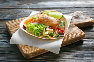 Wooden board with delicious fish taco on table