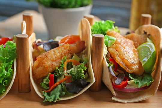 Wooden holder with delicious fish tacos on table, closeup