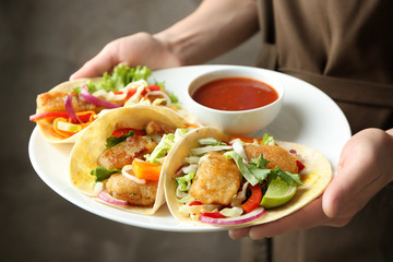 Woman holding plate with delicious fish tacos and tomato sauce, closeup