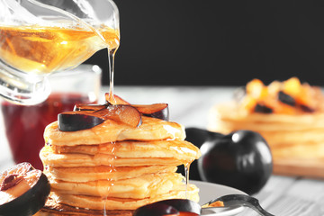 Pouring honey onto plate with tasty pancakes on table
