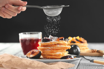 Woman decorating tasty pancakes with powdered sugar on table
