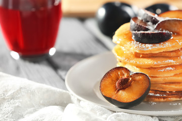 Plate with tasty pancakes and slices of plum on table