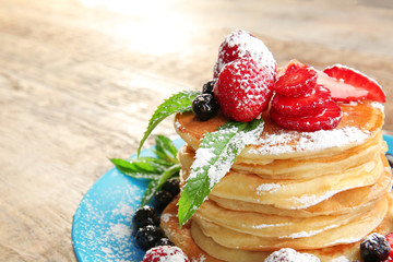 Plate with tasty pancakes and berries on wooden background