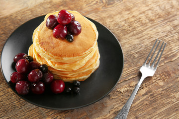 Plate with tasty pancakes and berries on wooden table