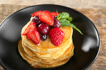 Plate with tasty pancakes and berries on wooden table, closeup