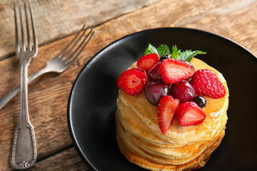Plate with tasty pancakes and berries on wooden table