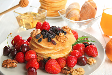 Plate with tasty pancakes, walnuts, raisins and berries on table