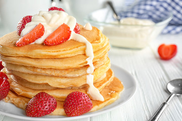 Plate with tasty pancakes, strawberry and sour cream on white wooden table
