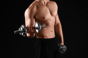 Fototapeta na wymiar Sporty young man doing exercise with dumbbells on black background