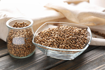 Glass jar and bowl with hemp seeds on wooden table