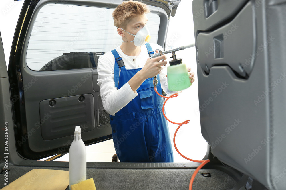 Wall mural Young man cleaning car salon in body shop