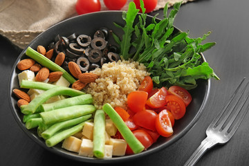 Plate with quinoa and vegetables on black background