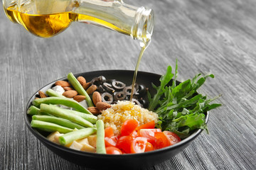 Adding oil to quinoa salad on wooden background