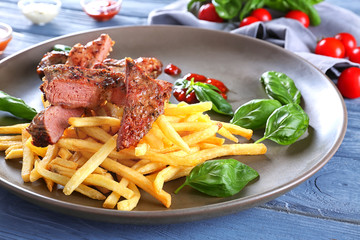 Plate with delicious grilled steak frites on wooden table
