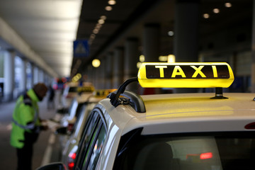 Taxischild auf Autodach mit Spiegelung, Schlange am Flughafen, Mann verteilt Tickets