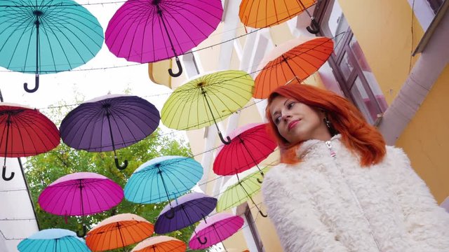 Beautiful red hair girl standing under color umbrellas roof at the street  
