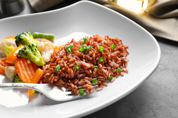Plate with tasty brown rice and vegetables on table