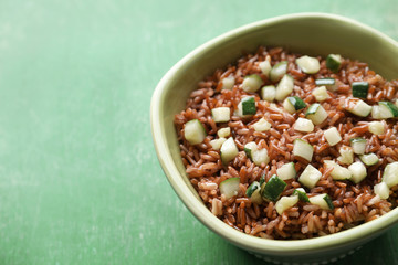 Bowl with tasty brown rice and zucchini on color wooden background