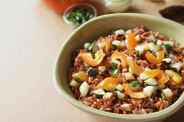 Bowl with tasty brown rice and vegetables on table