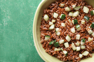 Bowl with tasty brown rice and zucchini on color wooden background